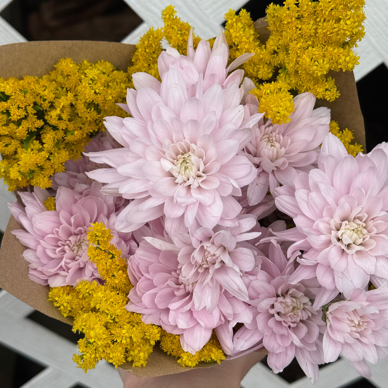 Bouquet of pink and yellow flowers in brown paper packaging.