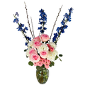 Bouquet of pink, white, and blue flowers in a clear vase on a white surface with a window in the background.