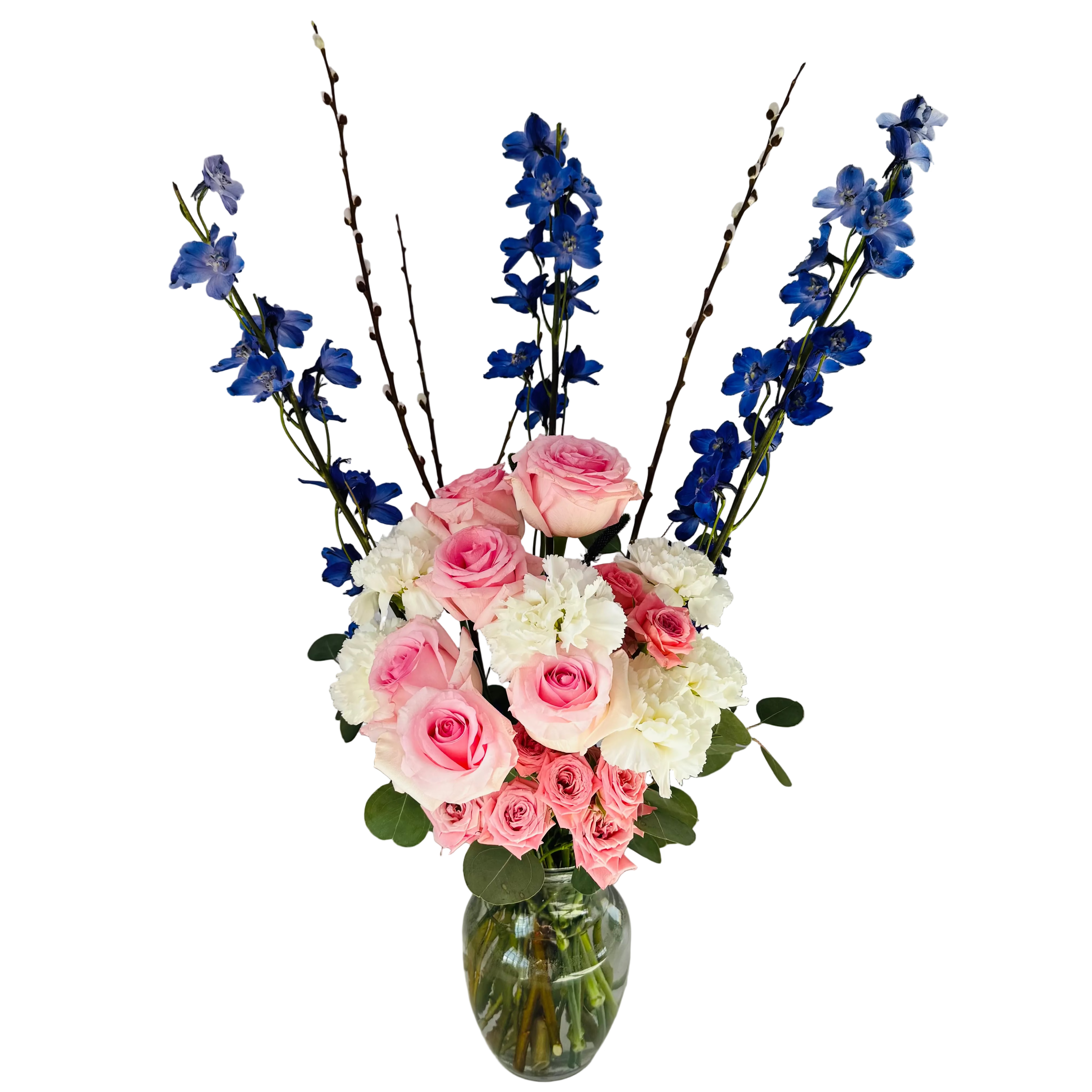Bouquet of pink, white, and blue flowers in a clear vase on a white surface with a window in the background.