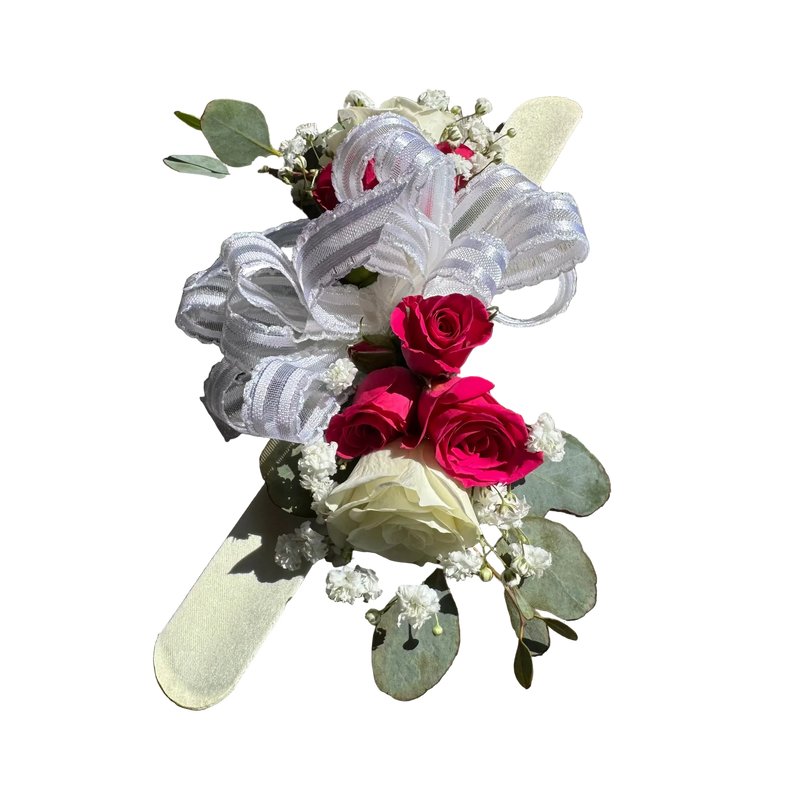 Floral corsage with red roses and white ribbons on a wooden surface